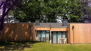Un bâtiment moderne en bois, doté d’un toit plat, de grandes fenêtres et d’un petit espace extérieur aménagé avec des chaises.