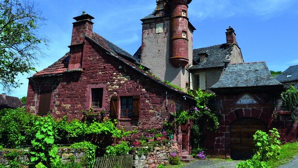 Un bâtiment historique en pierre, doté d’une tour imposante, de murs recouverts de lierre et d’une entrée rustique.