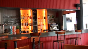 Un espace bar avec des étagères remplies de bouteilles et de verres, un appareil à café et des sièges avec des chaises et des tables.