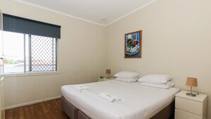 A hotel room with a bed, two bedside tables, a window with a blind, and a painting on the wall.