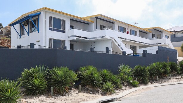 A modern two-story house with a prominent staircase, a balcony, and a well-maintained garden with agave plants.