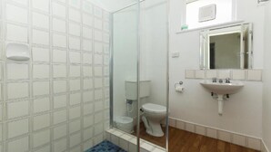 A bathroom with a glass shower enclosure, a white toilet, a sink with a mirror above it, and a tiled floor.