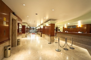 A hotel lobby with marble flooring, wooden reception desk, and a red carpet leading to the elevators.