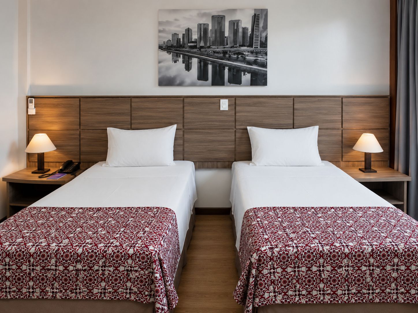 Ein Hotelzimmer mit zwei Betten, einem Stadtbild an der Wand und einem Holzkopfteil.