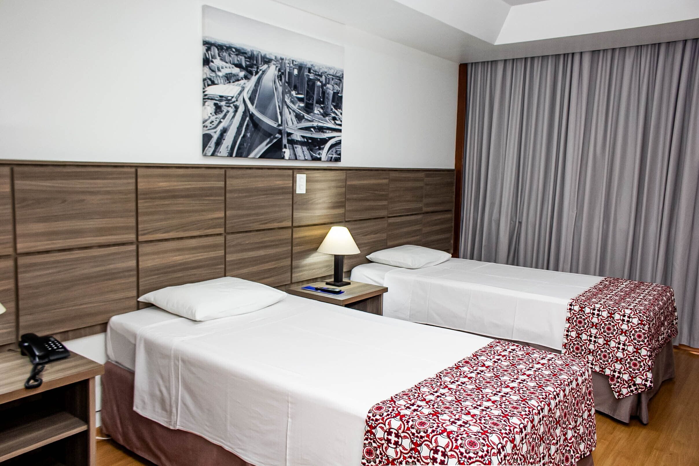 Habitación de hotel con dos camas, cabecero de madera, mesita de noche con lámpara, teléfono y un cuadro enmarcado en la pared.