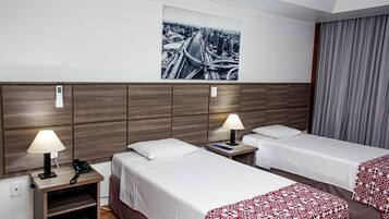 Hotellihuone, jossa on kaksi sänkyä, yöpöytä lampun kanssa, puhelin ja seinälle kiinnitetty taideteos.