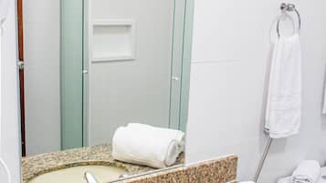 Casa de banho com bancada de granito, lavatório, espelho, cabine de duche em vidro e um porta-toalhas.
