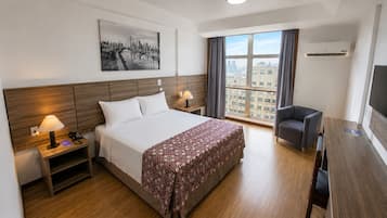 A hotel room with a bed, bedside tables, a desk, a chair, a TV, and a window with curtains.