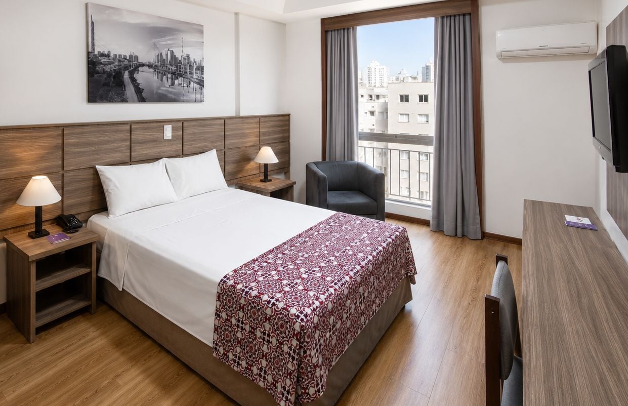 Ein Hotelzimmer mit Bett, Nachttischen, einem Sessel, einem Schreibtisch und einem Fernseher.