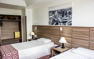 Camera d'albergo con due letti, una testiera in legno, un quadro con una veduta cittadina, un comodino con una lampada e un armadio.