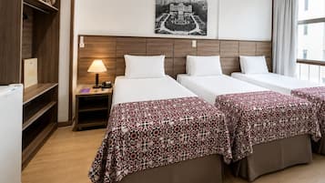 Et hotelværelse med to senge, et natbord, en lampe, et billede af en by udsigt og et vindue med gardiner.