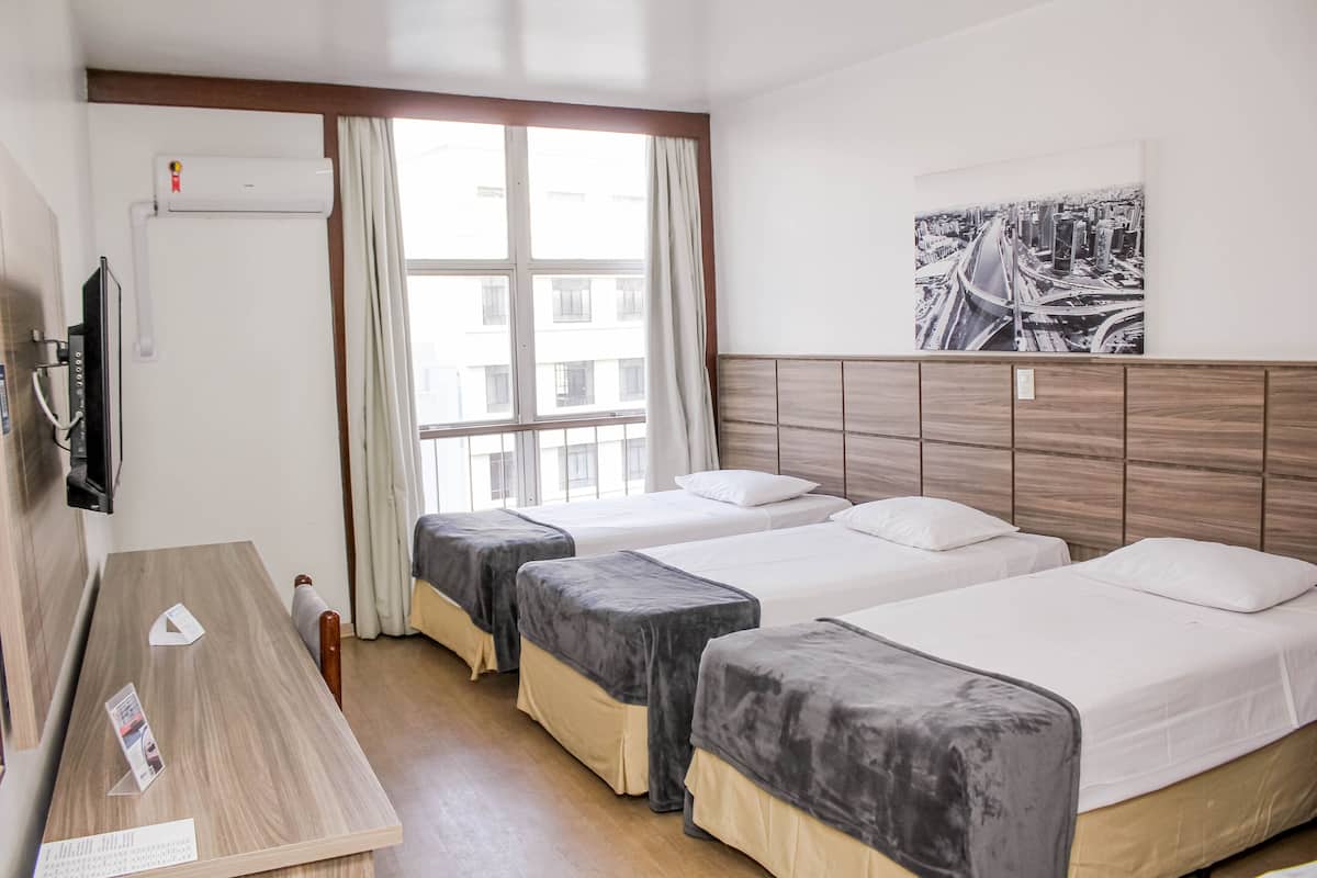 A hotel room with two beds, a wooden desk, a flat-screen TV, and a cityscape painting on the wall.
