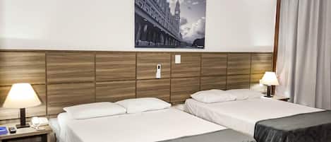 A hotel room with two beds, a wooden headboard, a painting of a bridge, and a nightstand with a lamp and phone.