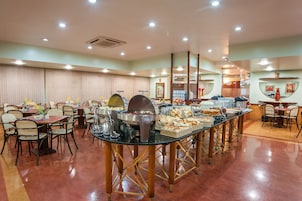 Disposição de buffet com diversas estações de serviço, mesas e cadeiras dispostas numa sala ampla.