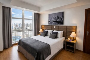 Camera d'albergo con un letto grande, due lampade ai comodini, vista sulla città e testiera in legno.