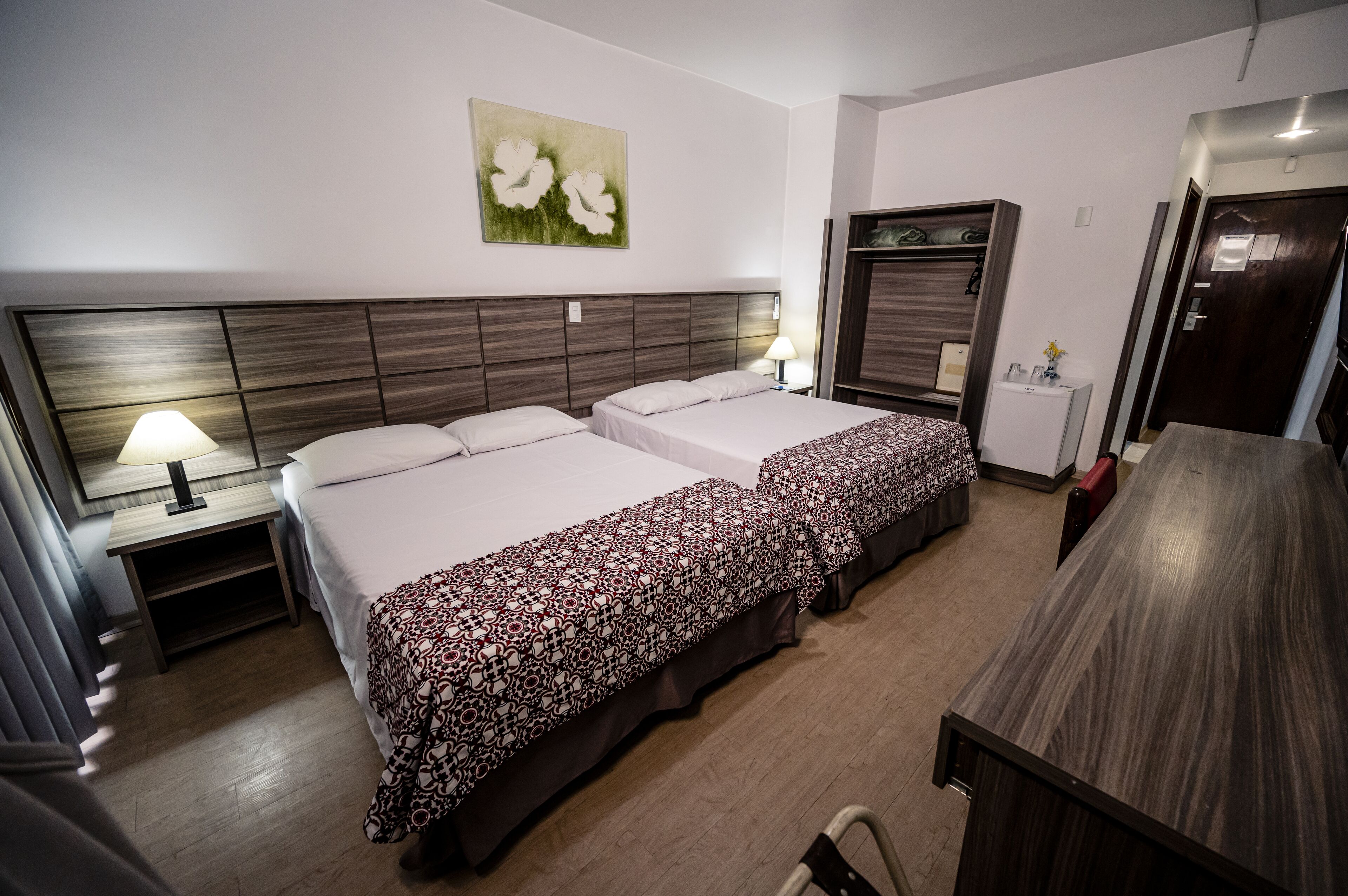 Una habitación de hotel con dos camas, un escritorio, una silla, una lámpara y un refrigerador pequeño.