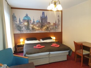 A hotel room with a bed, a desk, a chair, and a large cityscape painting on the wall.