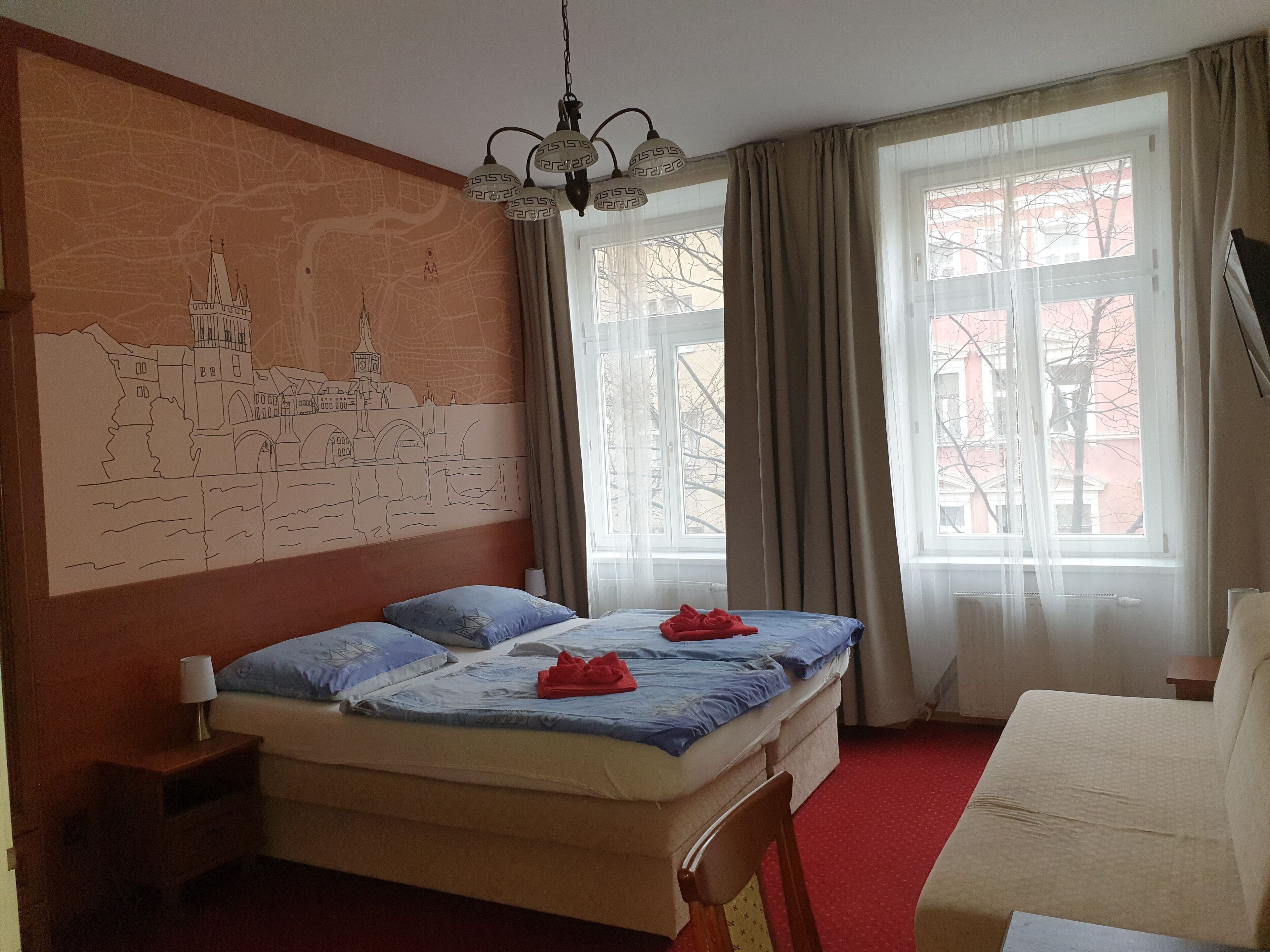 A hotel room with a bed, a nightstand, a chair, a large window with curtains, and a wall mural.
