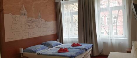 A hotel room with a bed, a nightstand, a chair, a large window with curtains, and a wall mural.
