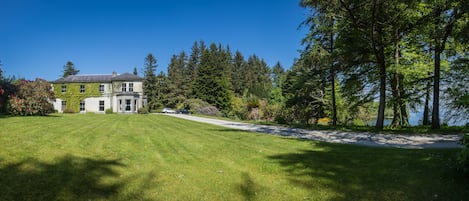 A large, two-story house with a well-maintained lawn and a driveway leading to a parked car.