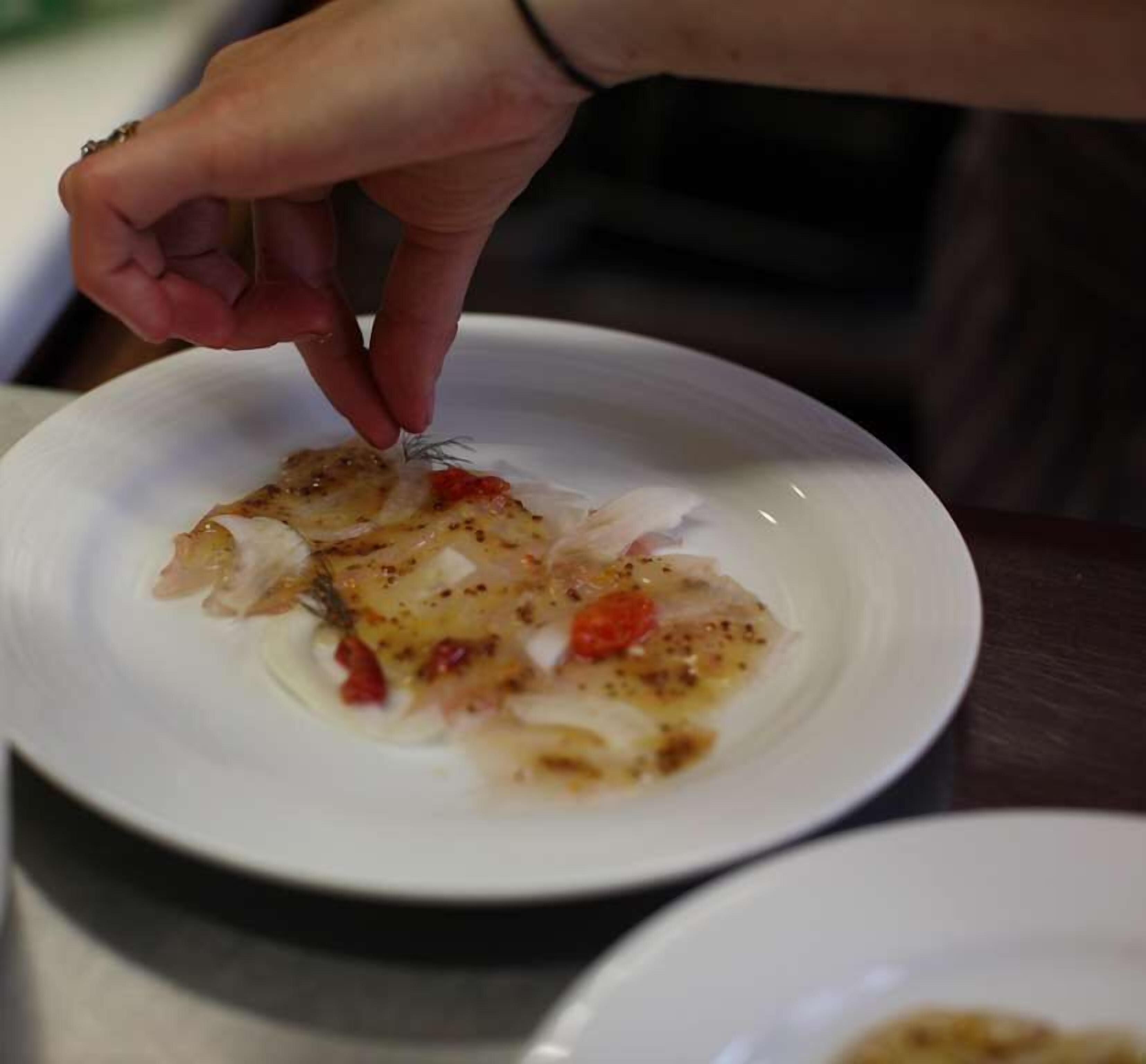 A hand placing a garnish on a plate of food.