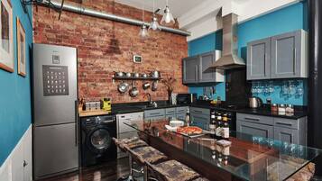 A modern kitchen with a brick wall, stainless steel appliances, and a glass island with bar stools.
