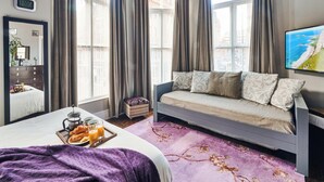Ein Hotelzimmer mit einem Bett, einer Couch, einem Frühstückswagen und einem großen Fenster mit Vorhängen.