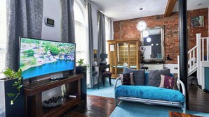 Ein Wohnzimmer mit Fernseher, Holzmöbeln, einem blauen Sofa und einer Backsteinwand.