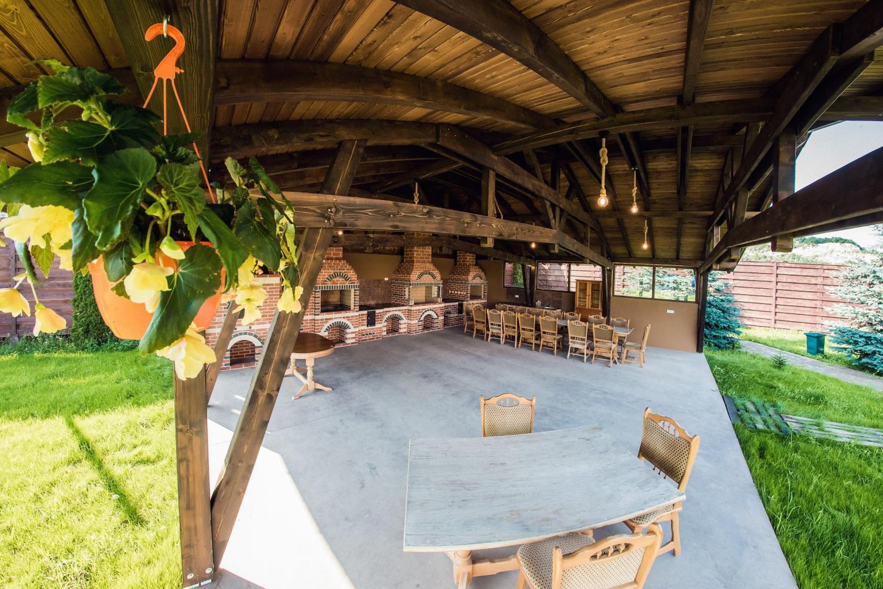 An outdoor patio area with brick barbecue grills, wooden tables and chairs, and hanging plants.