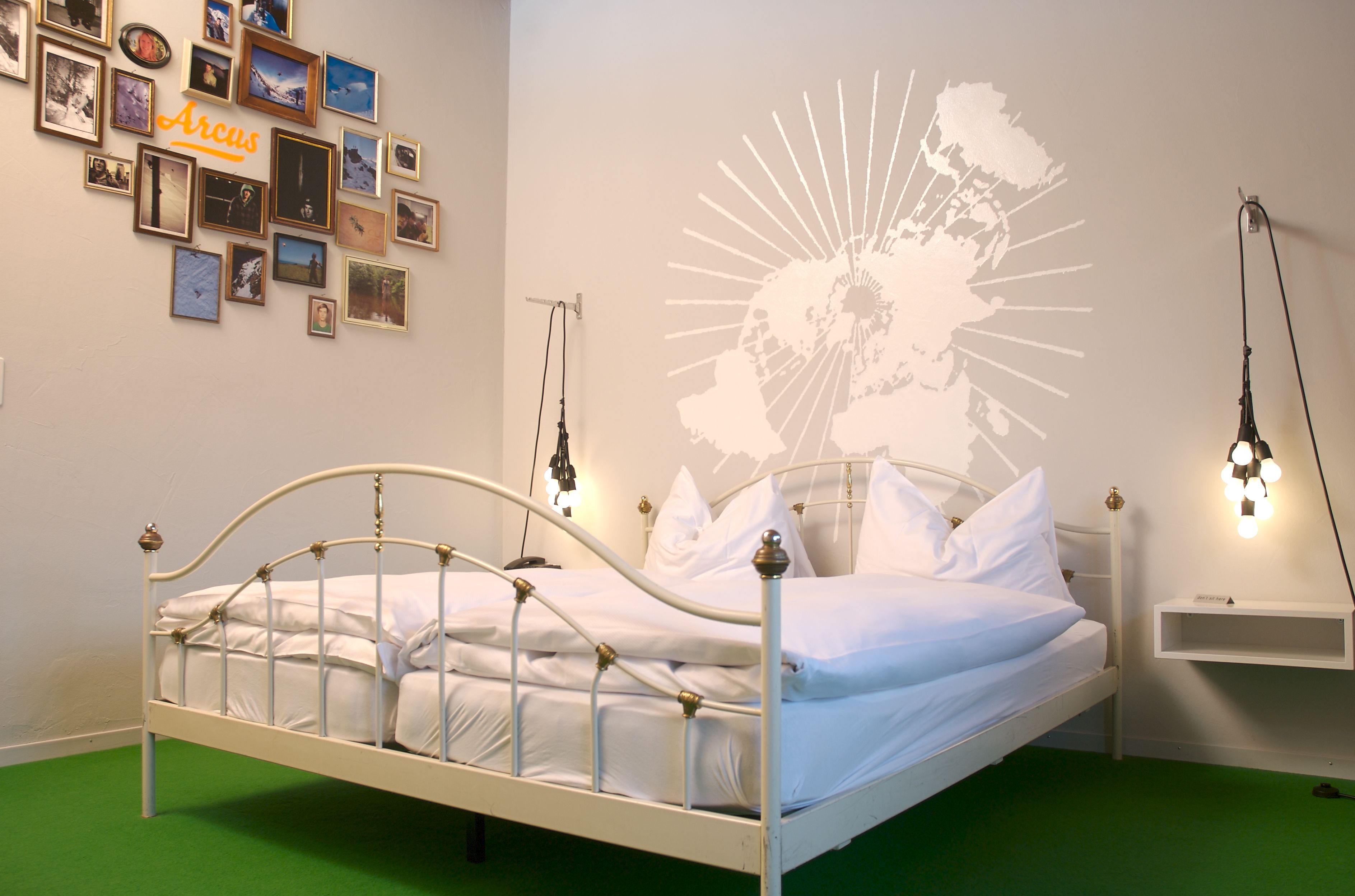 Una cama bien hecha en una habitación con alfombra verde, un muro decorado con fotos enmarcadas y una proyección de mapa.
