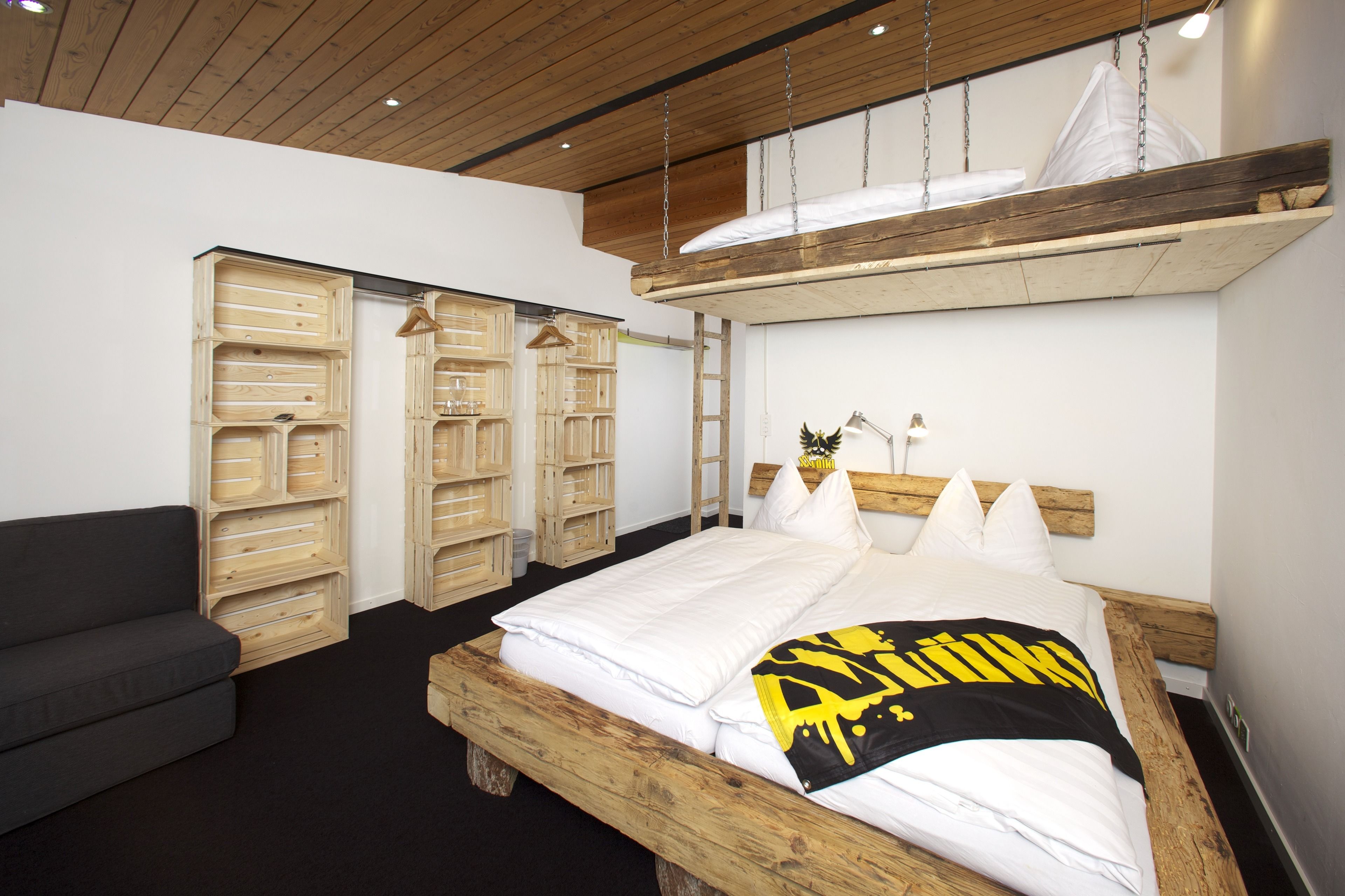 Un dormitorio con una cama de madera, un sofá gris y unidades de almacenamiento de madera.