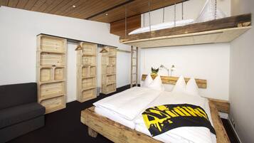 Un dormitorio con una cama de madera, un sofá gris y unidades de almacenamiento de madera.