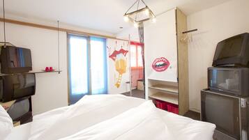 Ein Hotelzimmer mit einem Bett, zwei Fernsehern, einer Kristallleuchtre und einem roten Wandbild, sowie einem Fenster mit Vorhängen.