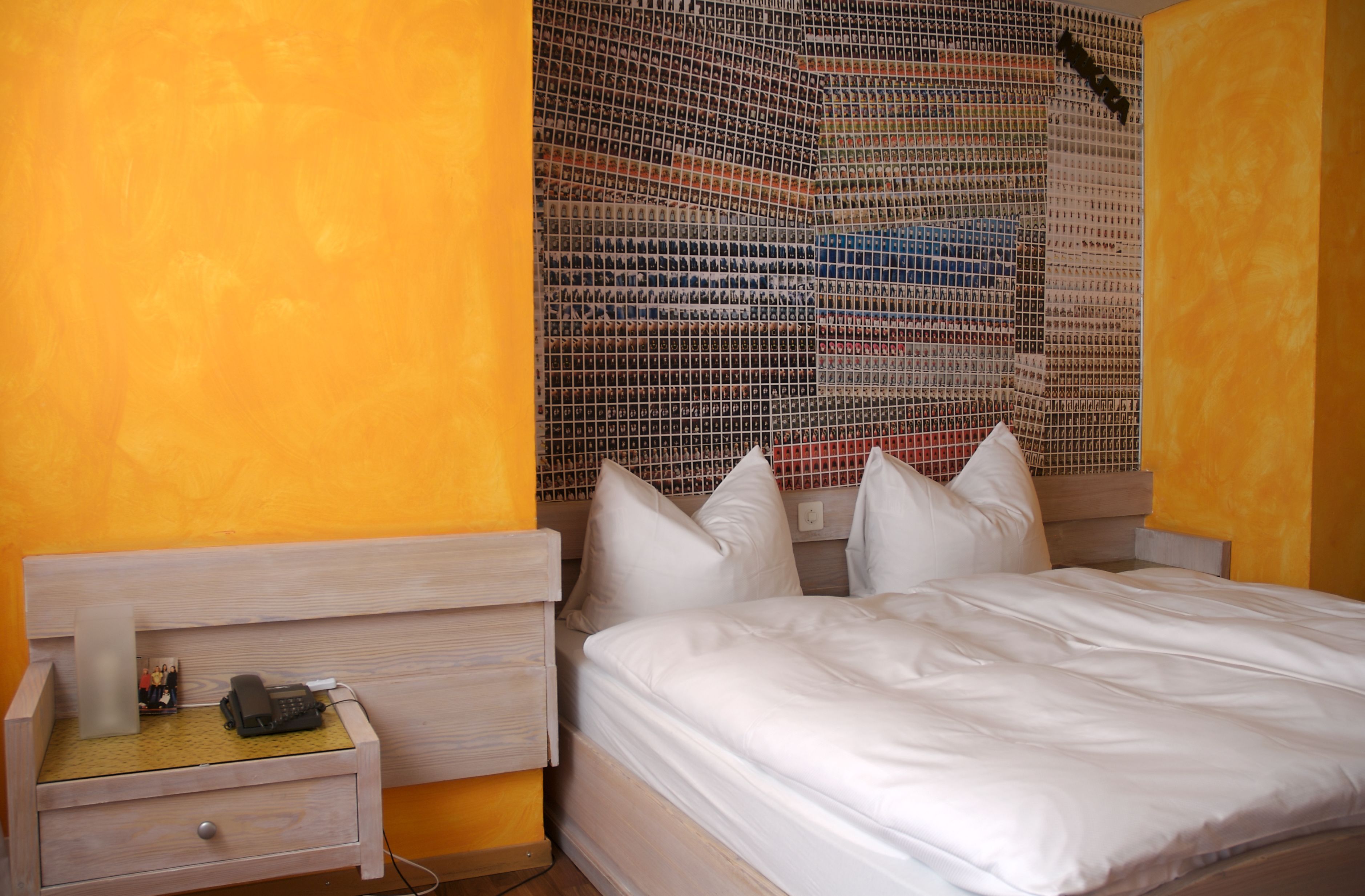 A hotel room with a bed, a nightstand with a phone and a lamp, and a wall with a patterned design.