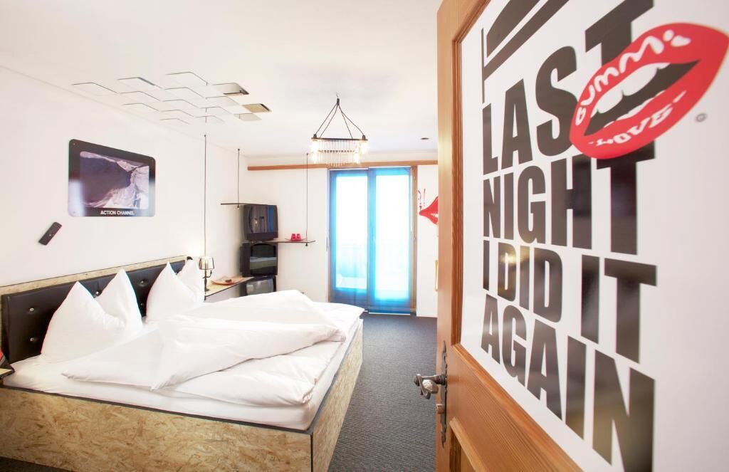 A hotel room with a bed, a television, a desk, and a door with a poster.