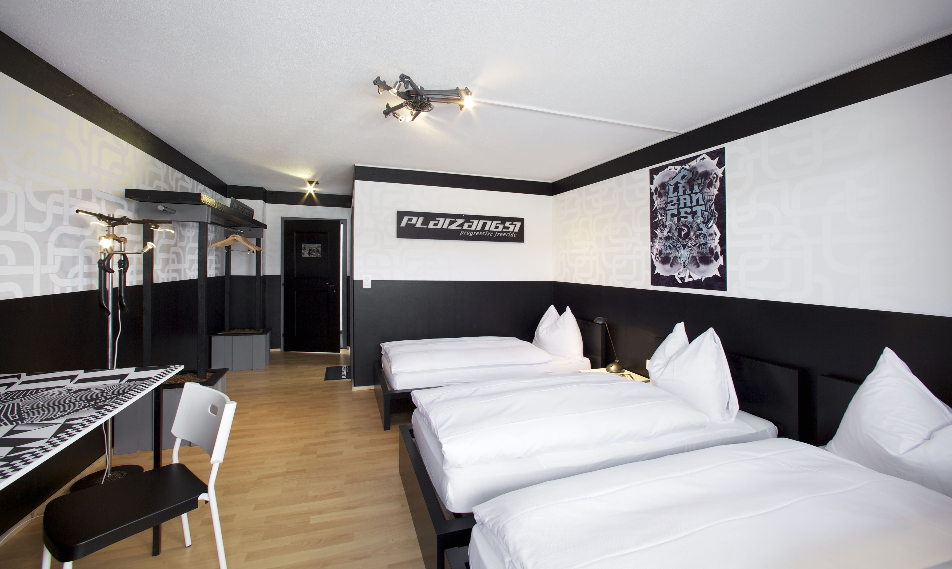 A hotel room with two beds, a desk, and a chair. There is a sign on the wall that reads "PLAZA 51 progressive freeride".