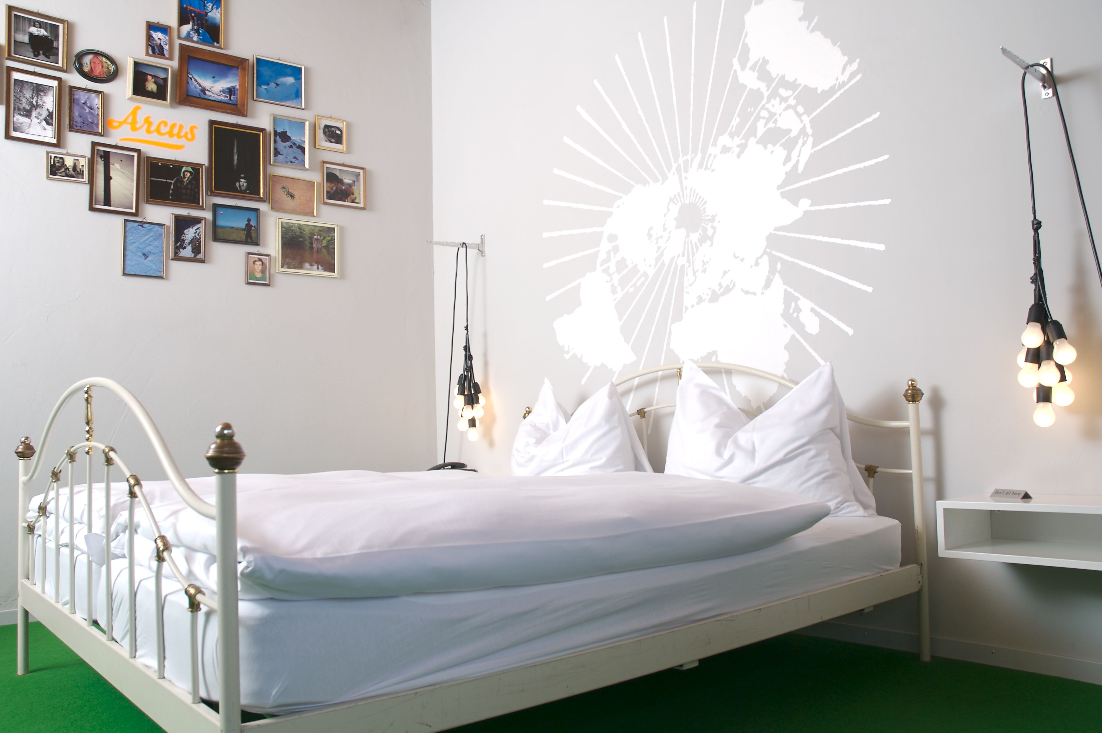 Una cama con ropa de cama blanca, una pared con fotos enmarcadas y una proyección cartográfica.