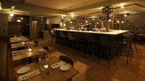 A modern bar area with a long counter, multiple stools, and a variety of bottles and glasses. - Arena Lodge (Flims)