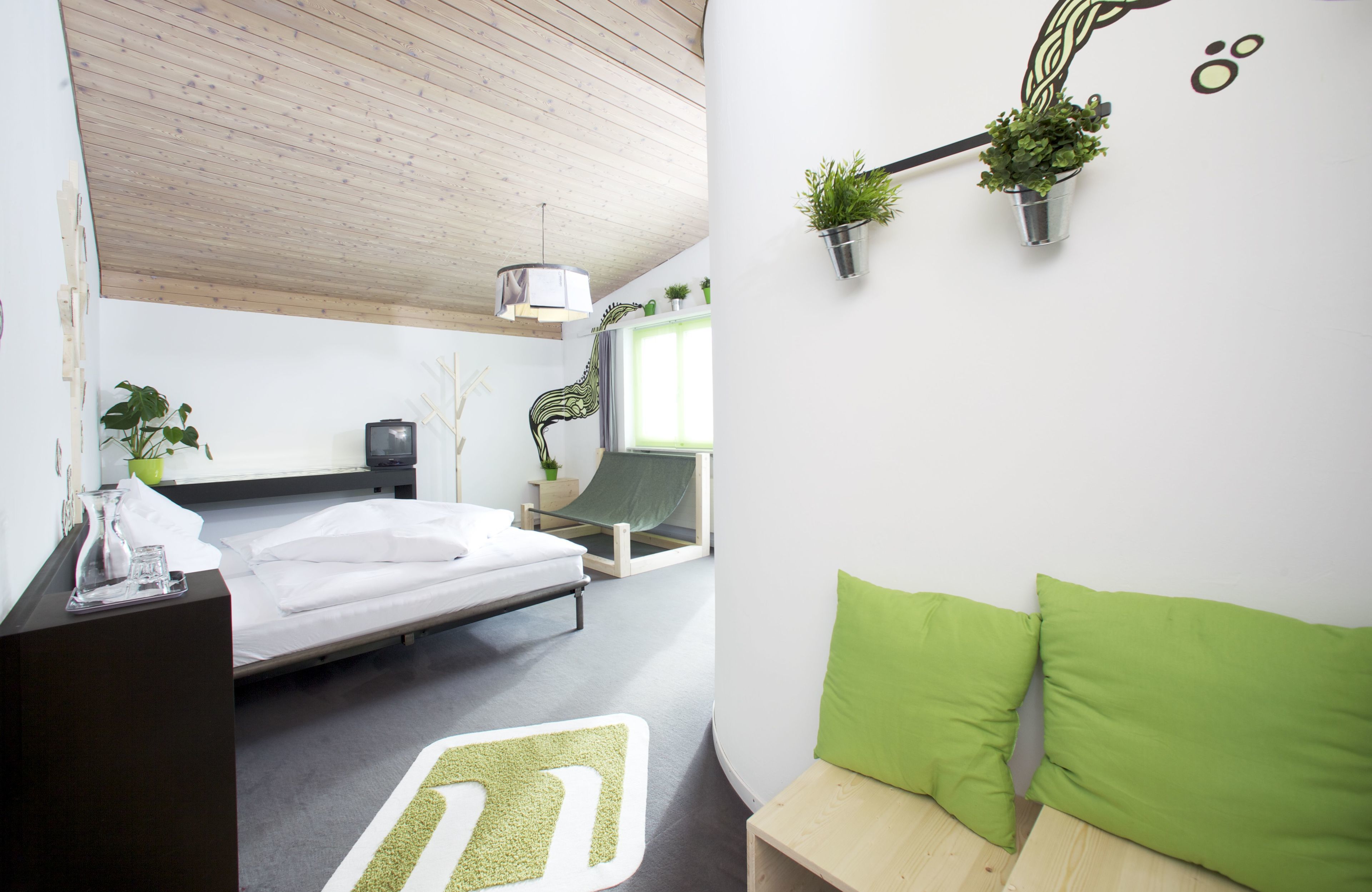 Et moderne hotelværelse med seng, skrivebord, grøn sofa og plantekasser.