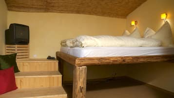 A single bed with white bedding, a television on a wooden stand, and a staircase with a red pillow.