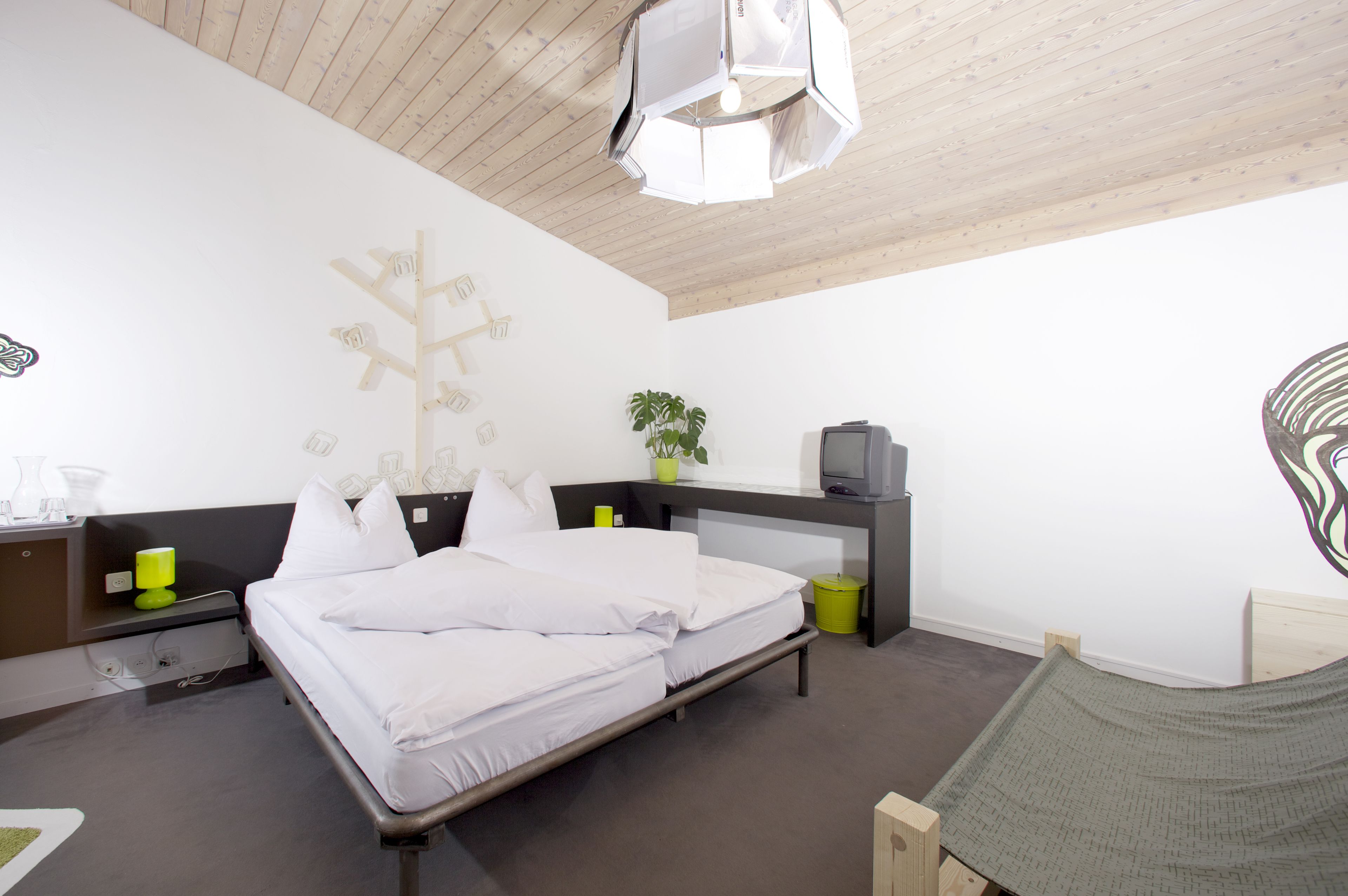 Un dormitorio moderno con cama, mesitas de noche, un escritorio, una silla, una lámpara colgante y una obra de arte en la pared.