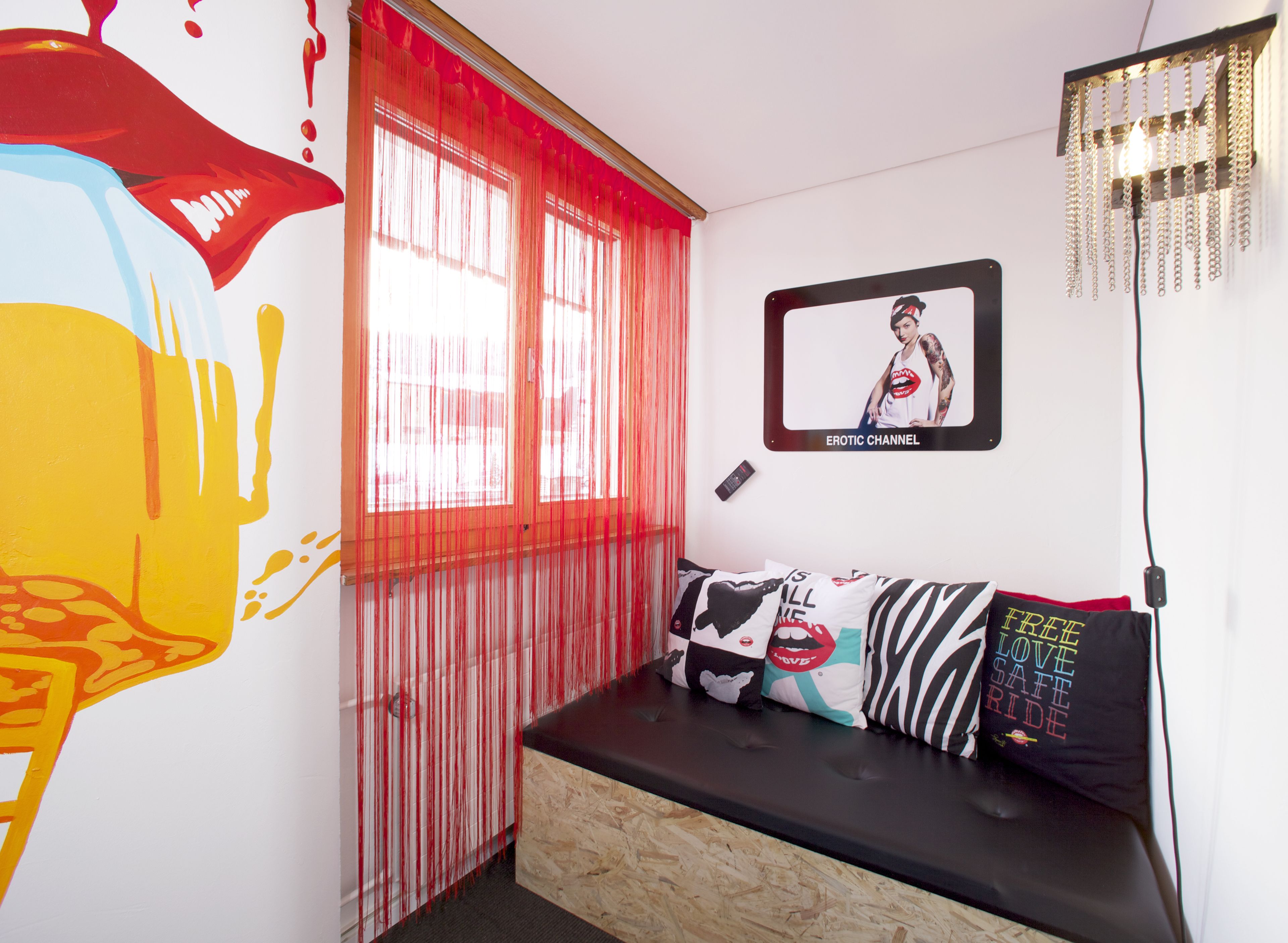 A room with a wooden bench, red curtains, a framed picture, and a wall with a colorful mural.