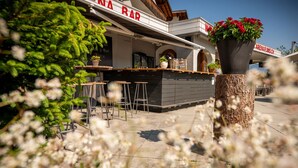 A restaurant with outdoor seating, a wooden bar counter, and a large planter with flowers. - Arena Lodge (Flims)