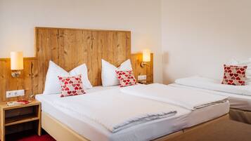 A hotel room with a wooden headboard, two beds, white bedding, and heart-patterned pillows.
