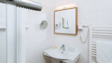 Un baño con lavamanos blanco, espejo y toallero.