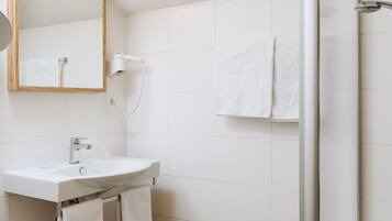 A bathroom with a white sink, a mirror, a hairdryer, and a shower.