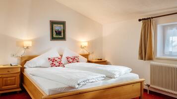 Een tweepersoonsbed met witte beddengoed, twee nachtkastjes met lampen, een lijst met een afbeelding aan de muur, een raam met gordijn, en een radiator.