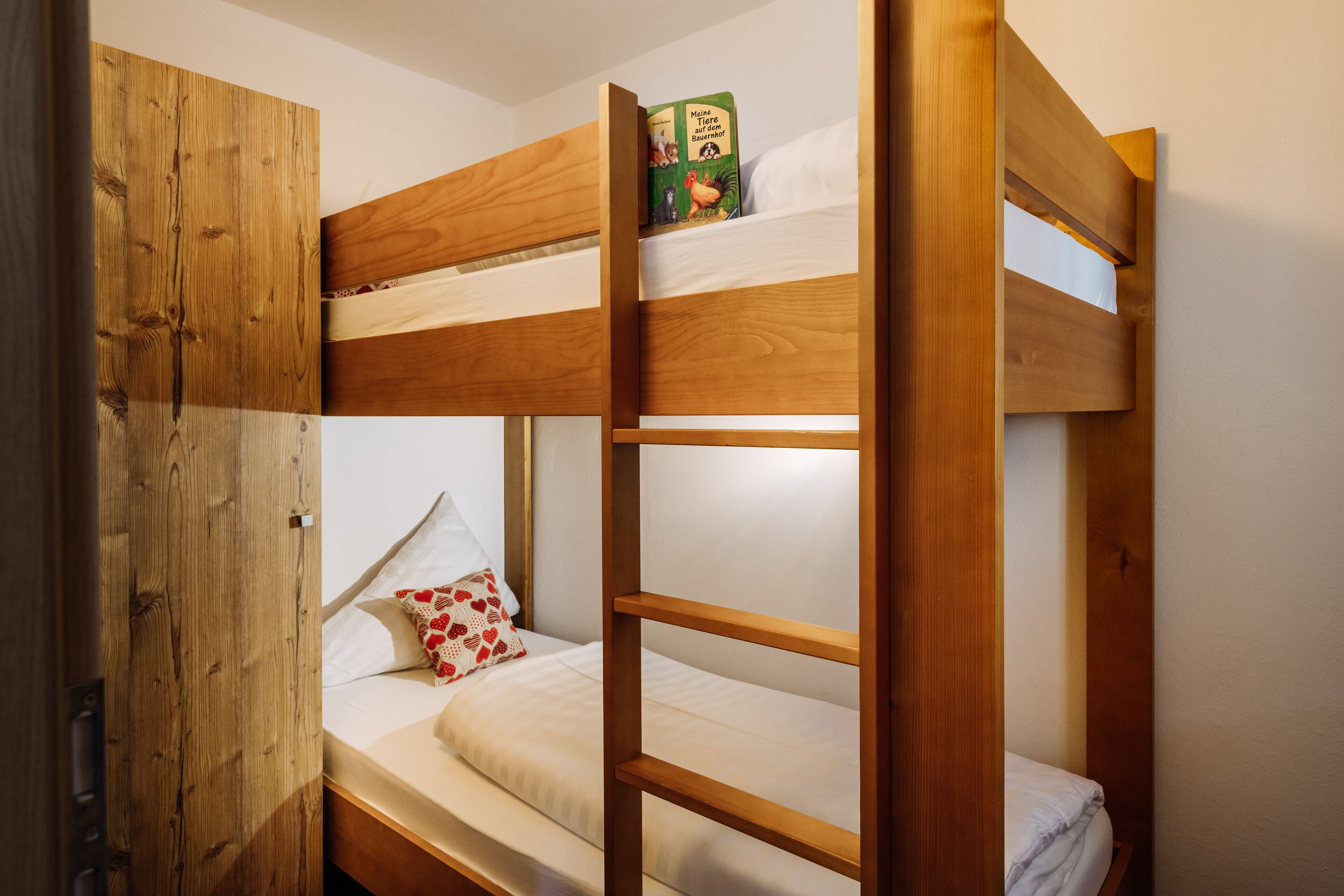 A bunk bed with a wooden headboard, a lower bed with a pillow, and a book on the top bunk.