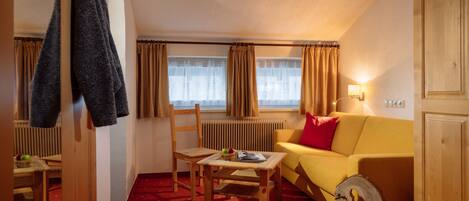 A cozy room with a yellow sofa, a wooden chair, a small table, and a radiator.