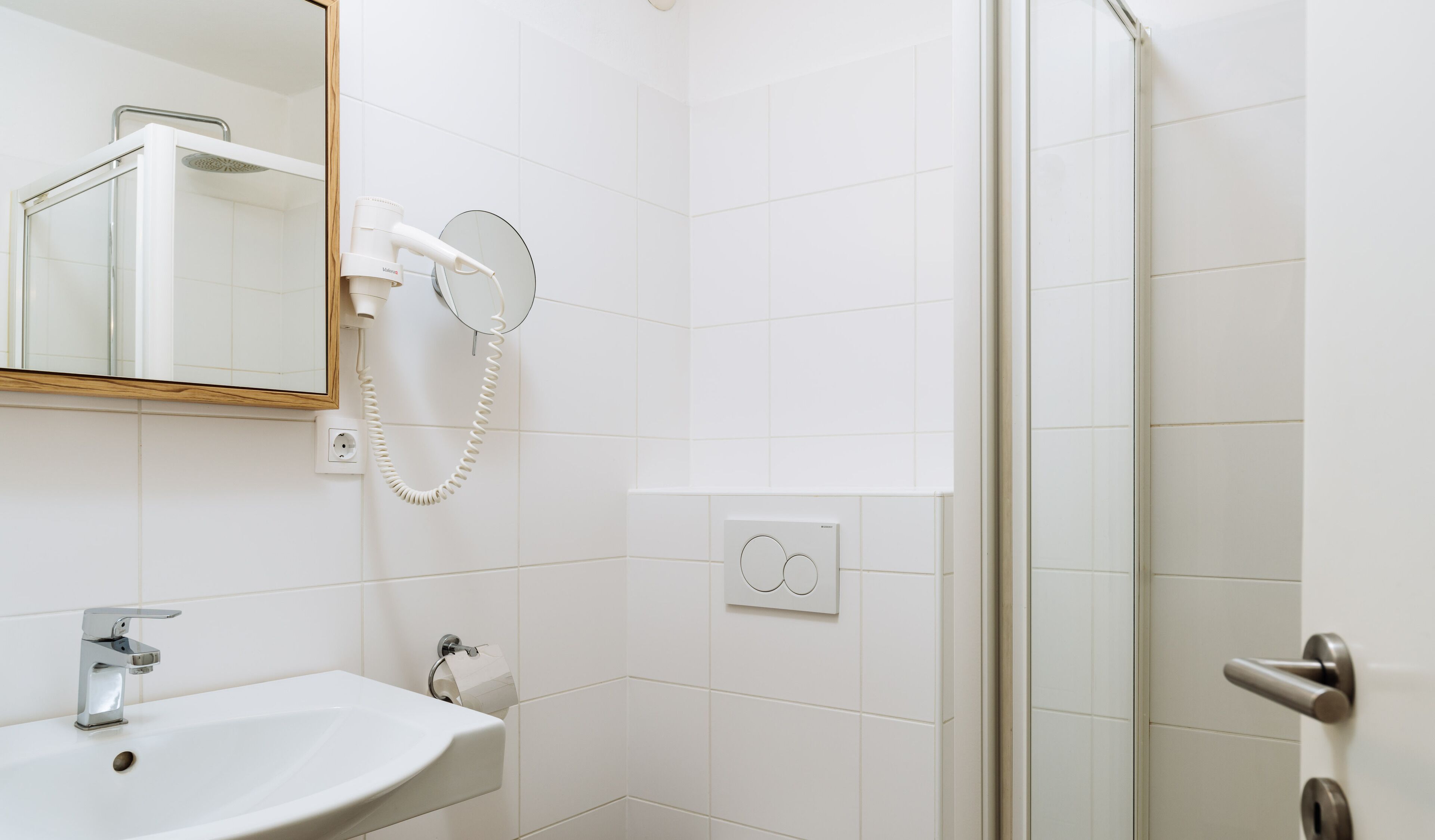 Un baño con lavamanos, espejo, secador de pelo y ducha.